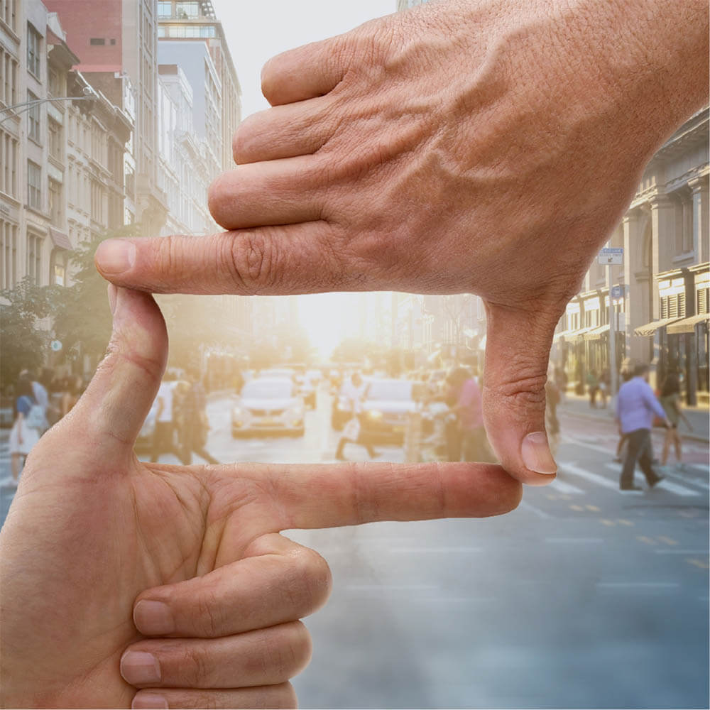 Person making a rectangle with their hands to make a frame around a busy street with cars and people