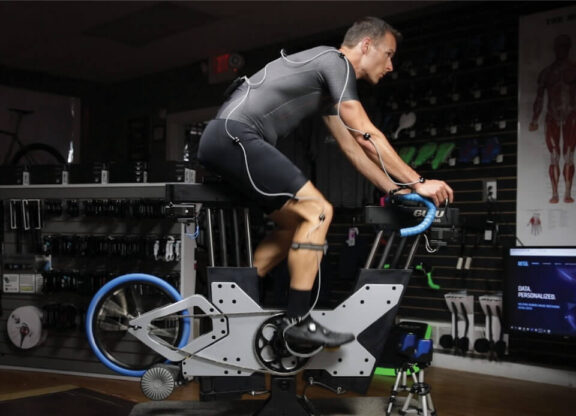 Photo of a man using a stationary bike with wires wrapped around his body while he peddles