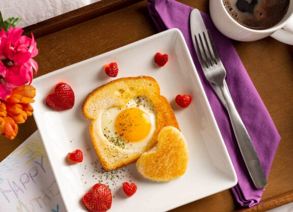 Photo of a white square plate that has strawberries shaped like hearts and toast with an egg in the middle shaped like a heart
