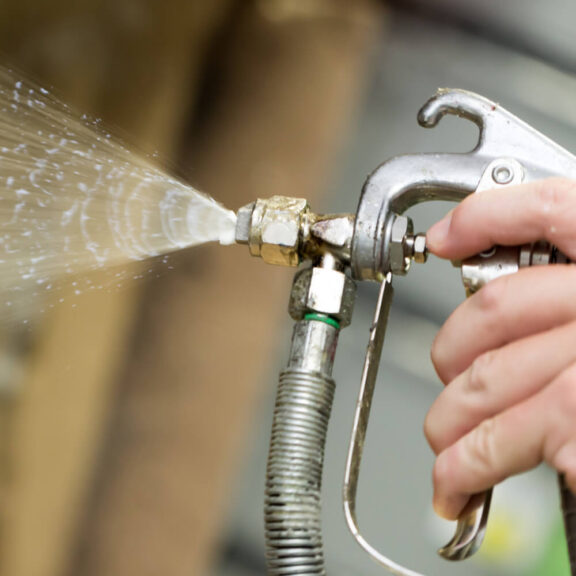 Close up photo of a person's hand holding a spray adhesive gun as adhesive sprays out of the nozzle
