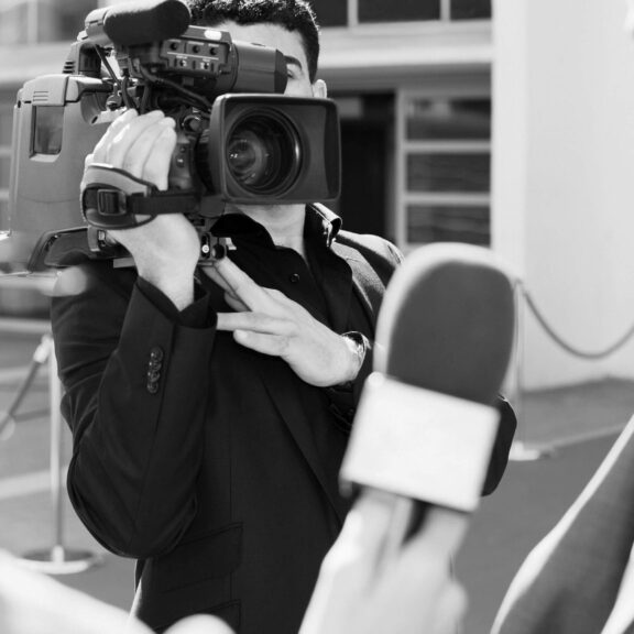 Black and white photo of a man holding a video camera for a news station