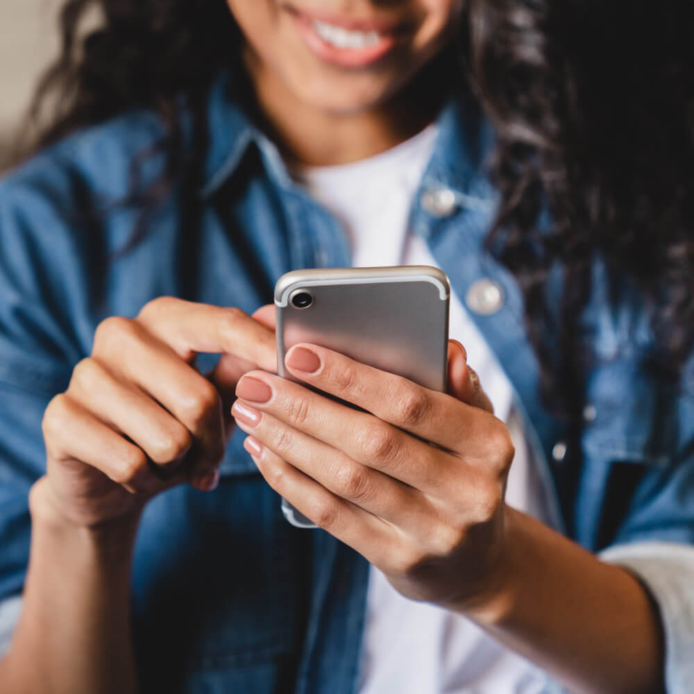 Woman in a jean jacket smiling and looking down at a phone as she scrolls with one hand