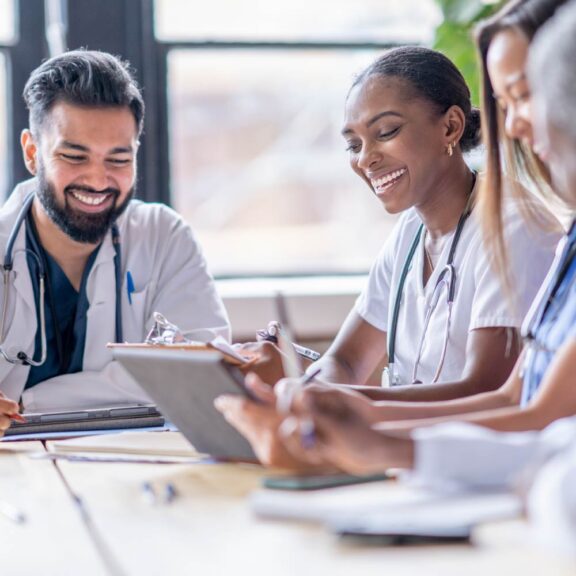 Photo of doctors sitting at a wooden table smiling while reviewing notes and information