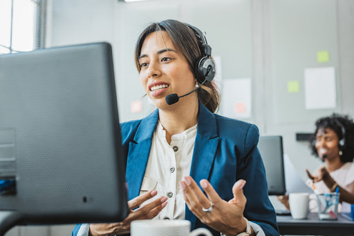 Photo of a female customer service representative smiling and looking at a computer monitor while wearing a headset