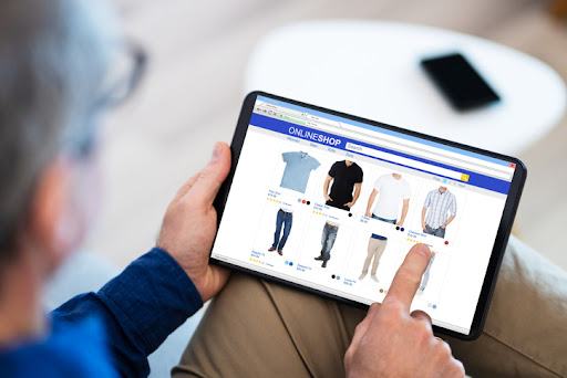 Image of a man wearing brown khaki pants and a long-sleeved navy blue shirt pointing with his finger at a shirt for sale on an online website