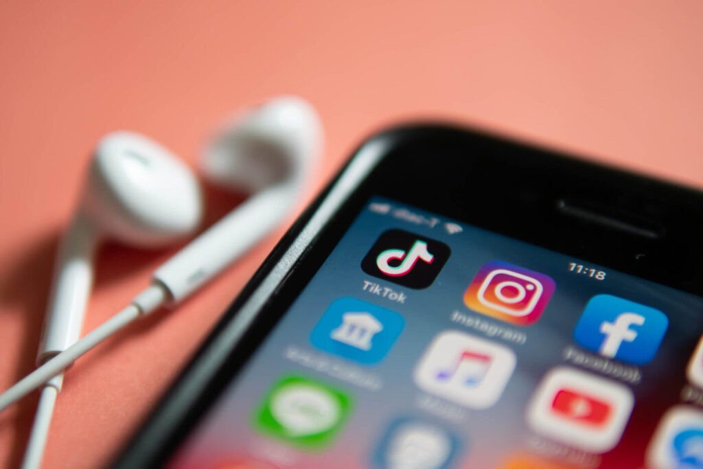 Image of a phone on a pink table with the TikTok app displayed on the screen and wired headphones sitting next to the phone